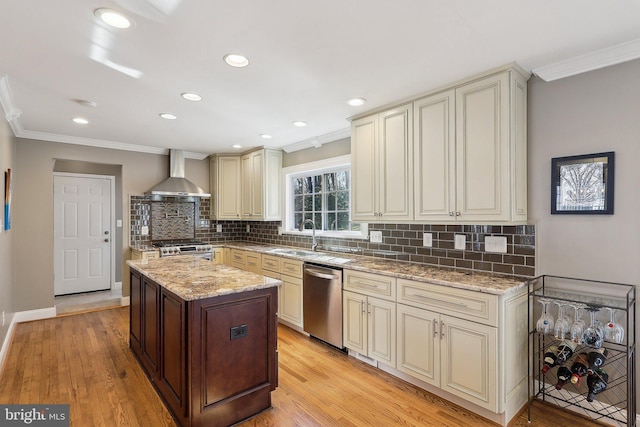 kitchen with wall chimney range hood, cream cabinets, stainless steel appliances, crown molding, and light wood finished floors