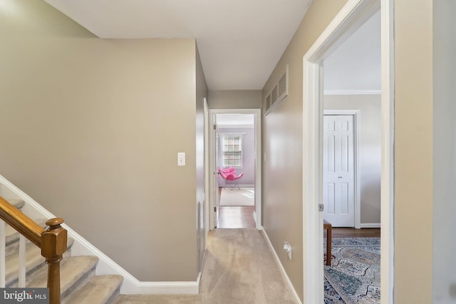 hallway featuring visible vents, baseboards, and light colored carpet