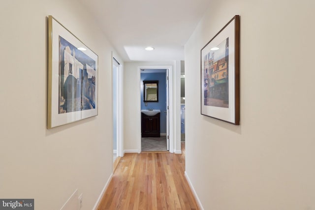 hall featuring recessed lighting, light wood-style floors, baseboards, and a sink