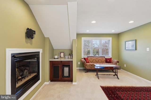 living area featuring recessed lighting, a glass covered fireplace, light colored carpet, and baseboards