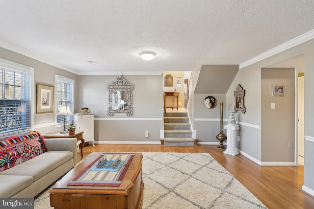 living area with ornamental molding, a textured ceiling, wood finished floors, stairway, and baseboards