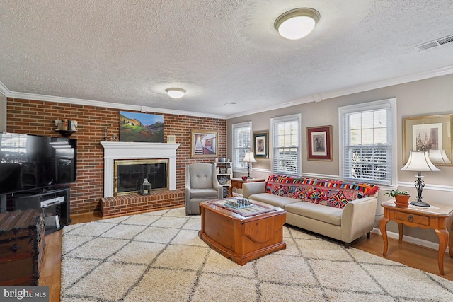 living area featuring wood finished floors, visible vents, wainscoting, crown molding, and a brick fireplace