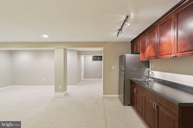 kitchen with dark countertops, baseboards, light colored carpet, freestanding refrigerator, and a sink