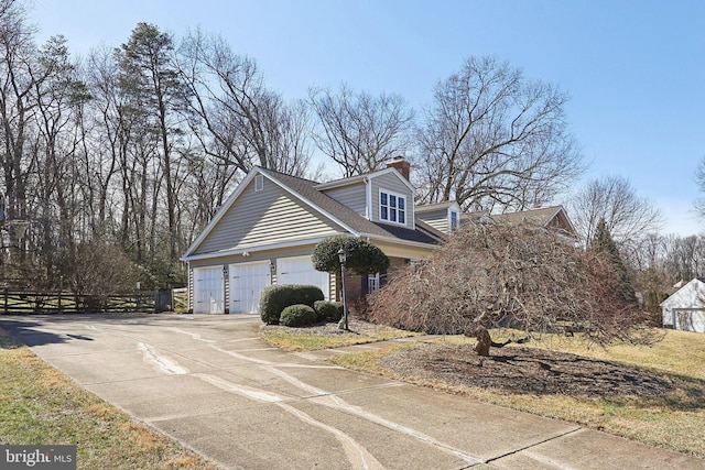 view of property exterior featuring driveway, a chimney, a garage, and fence