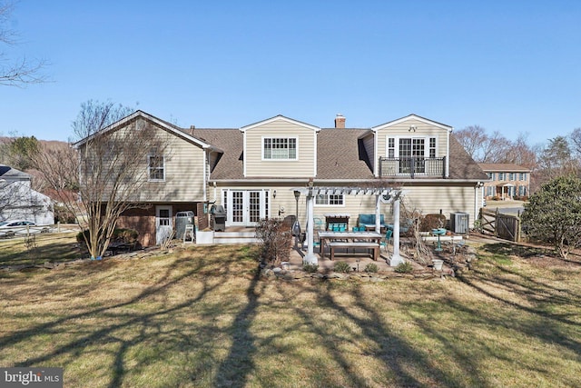 rear view of property with a balcony, fence, a yard, french doors, and a patio area