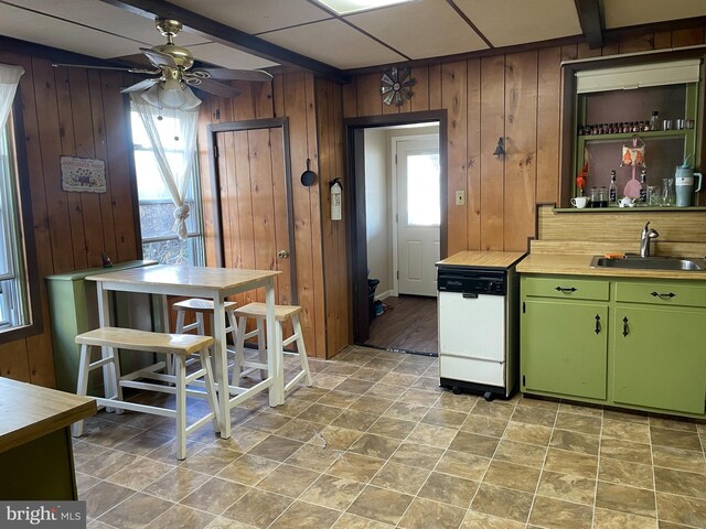 kitchen featuring wooden walls, a sink, green cabinets, dishwasher, and beamed ceiling