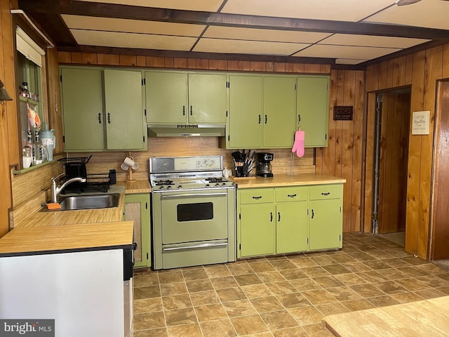 kitchen featuring white gas stove, light countertops, wood walls, a sink, and under cabinet range hood