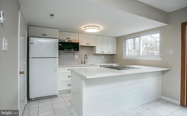 kitchen featuring decorative backsplash, stainless steel microwave, freestanding refrigerator, light countertops, and a sink