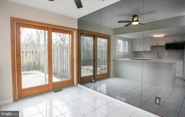 interior space with light tile patterned floors, backsplash, ceiling fan, a sink, and baseboards