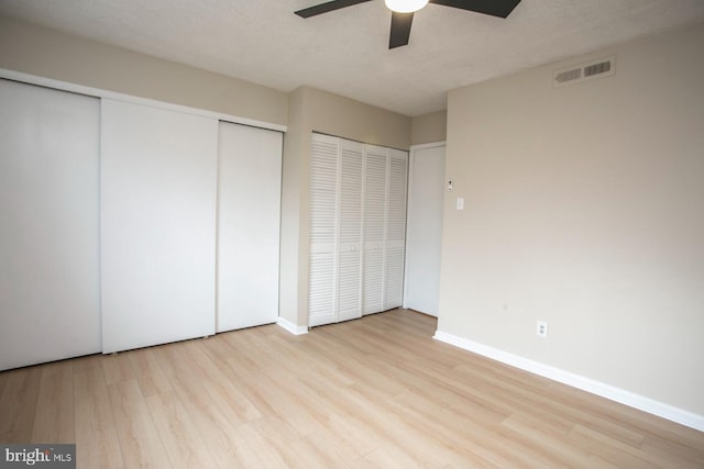 unfurnished bedroom with baseboards, visible vents, wood finished floors, a textured ceiling, and multiple closets