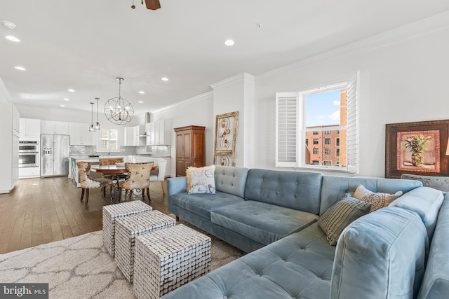 living area featuring recessed lighting, crown molding, hardwood / wood-style floors, and ceiling fan with notable chandelier