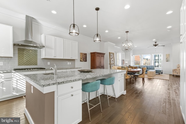 kitchen with decorative backsplash, wood-type flooring, white cabinets, and wall chimney exhaust hood