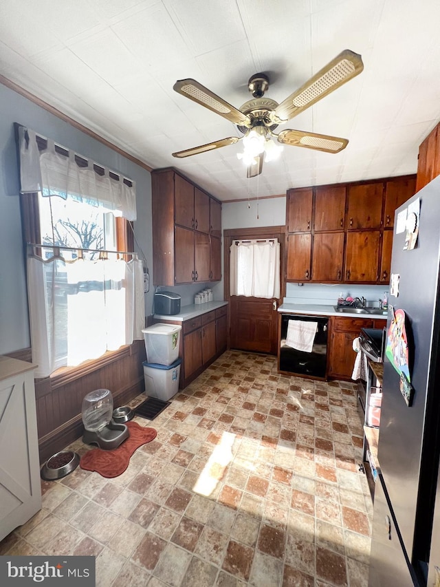 kitchen with black dishwasher, light countertops, a ceiling fan, freestanding refrigerator, and wooden walls