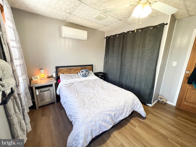 bedroom featuring a wall unit AC, ceiling fan, baseboards, and wood finished floors