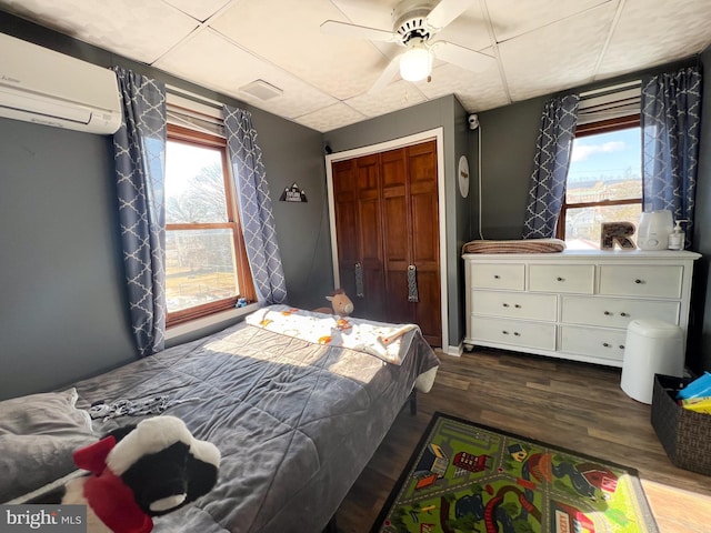 bedroom featuring dark wood-type flooring, an AC wall unit, multiple windows, and a closet