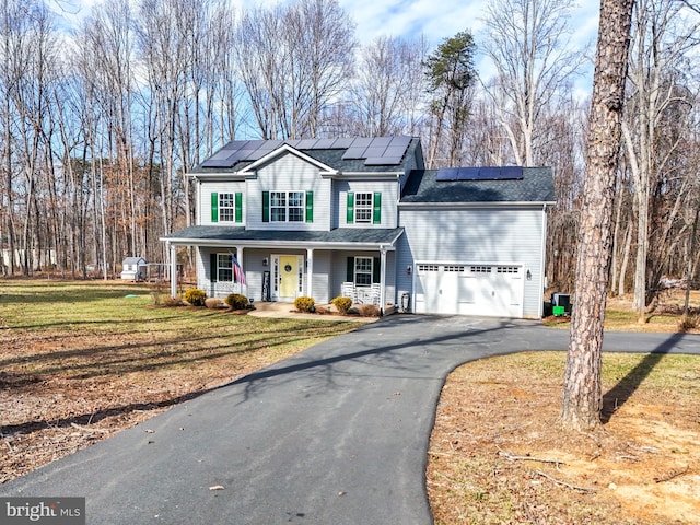 traditional home with aphalt driveway, solar panels, covered porch, an attached garage, and a front yard