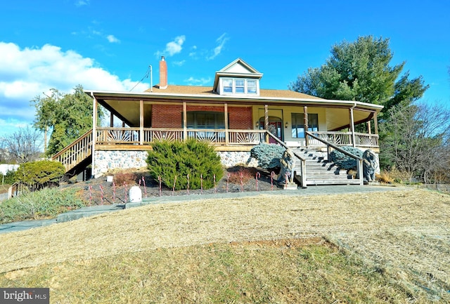 farmhouse-style home with stairs, a porch, a front yard, and brick siding