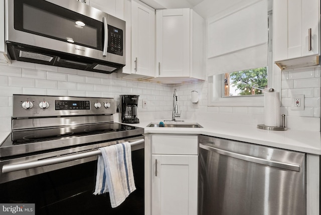 kitchen with stainless steel appliances, light countertops, decorative backsplash, white cabinetry, and a sink