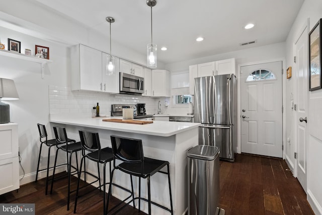 kitchen with stainless steel appliances, a peninsula, light countertops, and white cabinetry