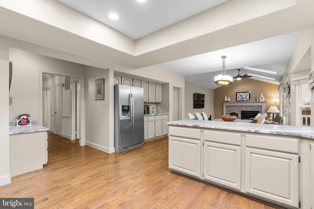 kitchen with a fireplace, light wood finished floors, light countertops, vaulted ceiling, and stainless steel fridge