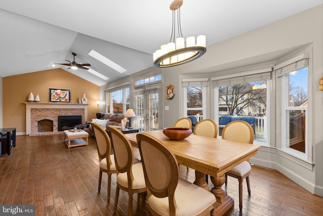 dining space featuring vaulted ceiling with skylight, a healthy amount of sunlight, a fireplace, and dark wood finished floors