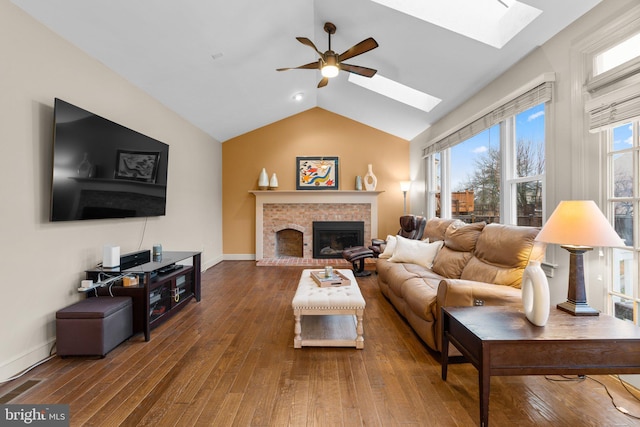 living area featuring vaulted ceiling with skylight, a brick fireplace, wood-type flooring, and a wealth of natural light