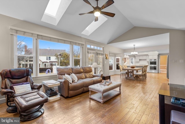 living area with high vaulted ceiling, light wood-type flooring, ceiling fan, and a skylight