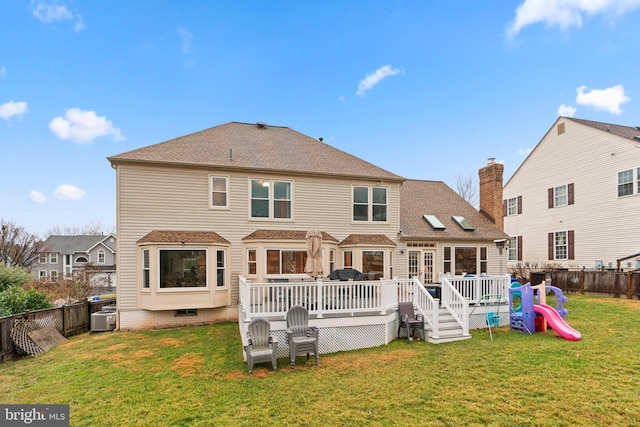 rear view of property with a fenced backyard, a yard, a deck, and a playground