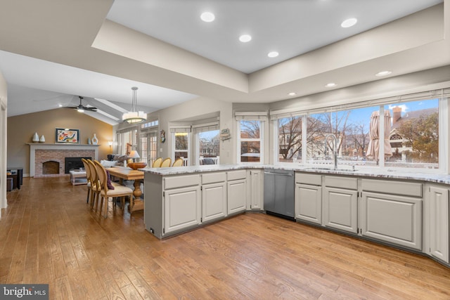 kitchen featuring lofted ceiling, light wood-type flooring, stainless steel dishwasher, a fireplace, and a sink