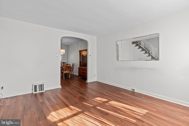 empty room featuring arched walkways, visible vents, baseboards, and wood finished floors