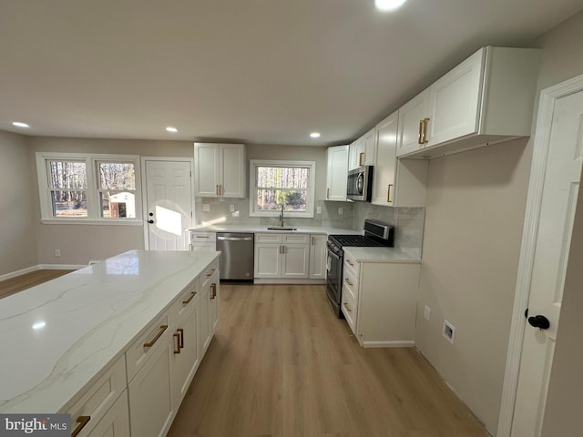 kitchen with light stone counters, stainless steel appliances, tasteful backsplash, light wood-style flooring, and a sink