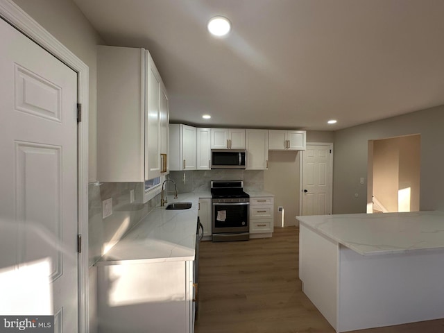 kitchen with decorative backsplash, appliances with stainless steel finishes, light stone counters, white cabinetry, and a sink