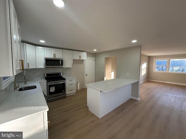 kitchen with light wood-style flooring, appliances with stainless steel finishes, a sink, light stone countertops, and a peninsula