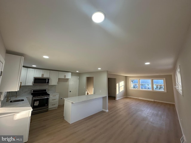 kitchen featuring light wood finished floors, stainless steel appliances, light countertops, white cabinets, and a sink