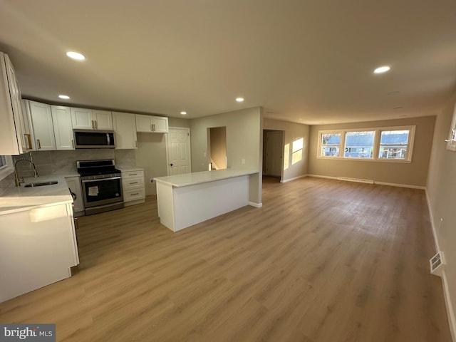 kitchen featuring light wood-style floors, appliances with stainless steel finishes, open floor plan, and a sink