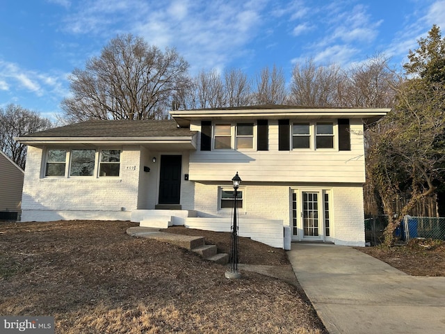 tri-level home featuring cooling unit, brick siding, and fence