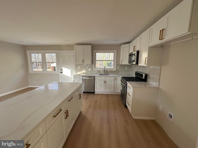 kitchen with tasteful backsplash, appliances with stainless steel finishes, light wood-type flooring, white cabinetry, and a sink