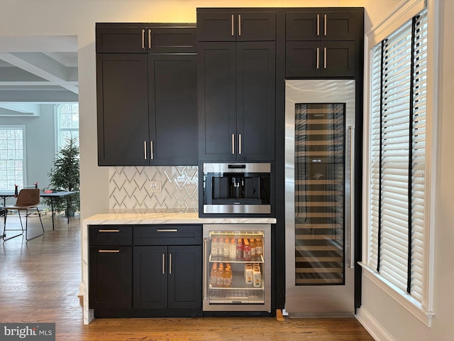 bar featuring light wood-style floors, beverage cooler, tasteful backsplash, and oven