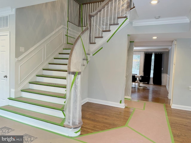 stairway featuring recessed lighting, a decorative wall, crown molding, and wood finished floors