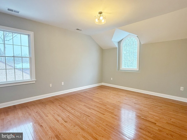 additional living space with light wood-style flooring, visible vents, vaulted ceiling, and baseboards