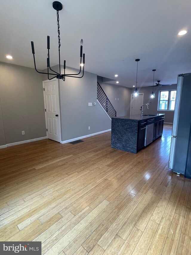kitchen with wood finished floors, open floor plan, a sink, decorative light fixtures, and stainless steel appliances