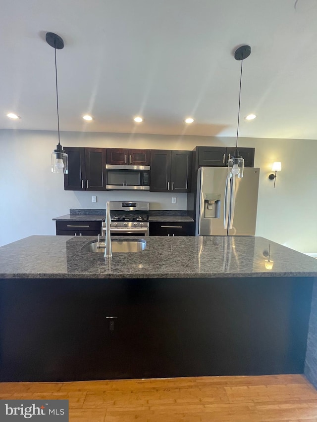 kitchen featuring dark stone counters, appliances with stainless steel finishes, hanging light fixtures, and a sink
