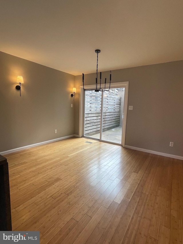 unfurnished dining area featuring baseboards, light wood finished floors, and a chandelier