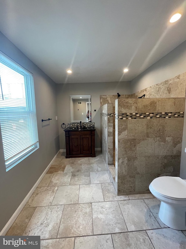 bathroom with walk in shower, vanity, baseboards, toilet, and stone tile floors