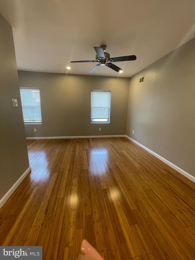 empty room featuring baseboards, ceiling fan, hardwood / wood-style floors, and visible vents