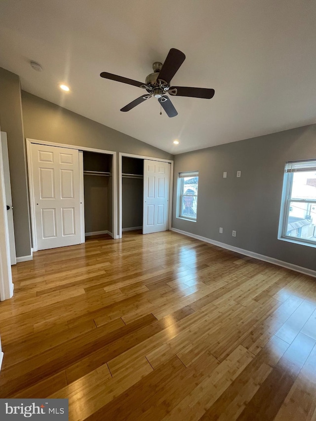 unfurnished bedroom with multiple closets, baseboards, wood finished floors, and lofted ceiling