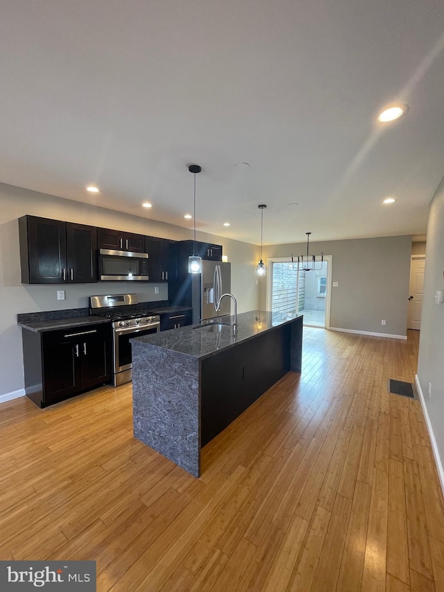 kitchen featuring baseboards, light wood-type flooring, dark cabinets, a sink, and appliances with stainless steel finishes