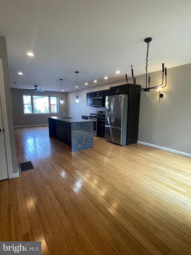 kitchen with appliances with stainless steel finishes, light wood finished floors, open floor plan, dark cabinetry, and recessed lighting