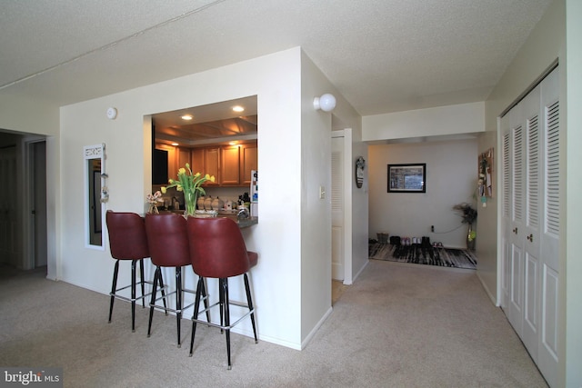 kitchen featuring a raised ceiling, a breakfast bar area, brown cabinets, and light colored carpet