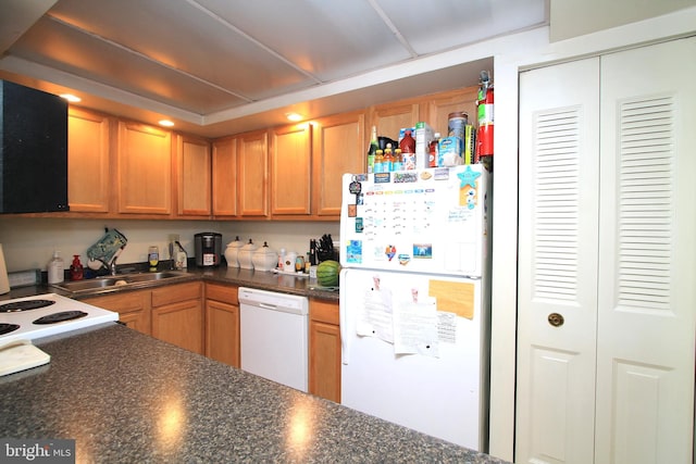 kitchen with dark countertops, white appliances, and a sink